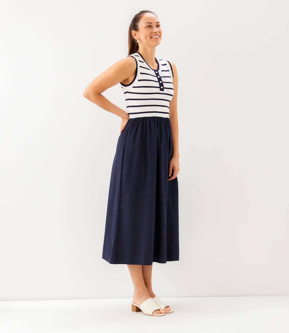 Woman wearing a black and white striped sleeveless top with a navy blue skirt on a white background
