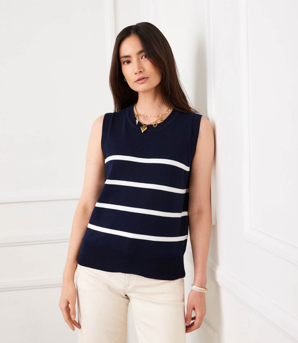 Woman wearing a navy sleeveless sweater with white stripes against a white background