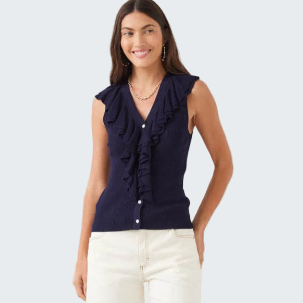 Woman wearing a navy blue ruffled top with white pants on a light gray background