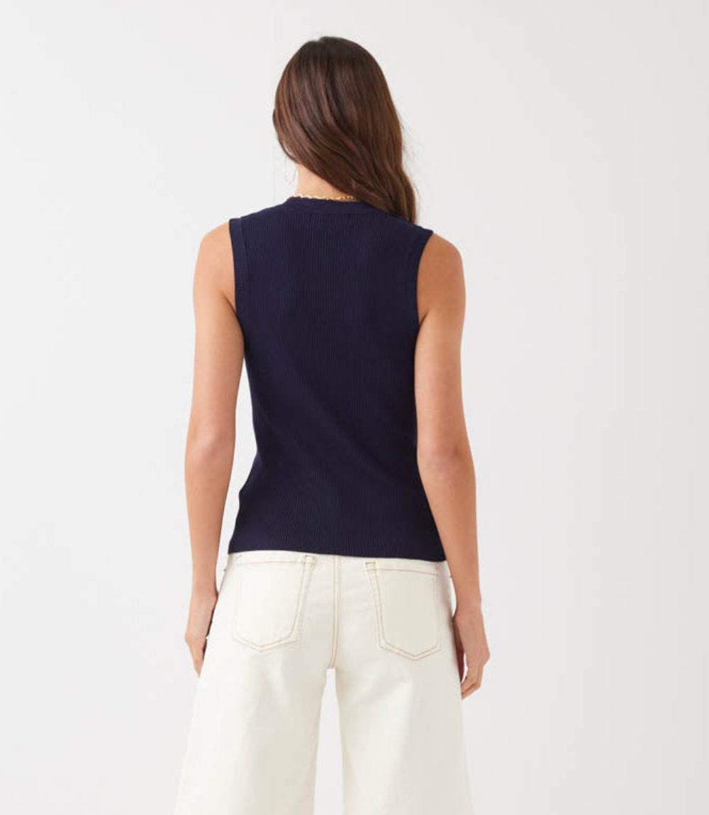 Person wearing a navy sleeveless top and white pants on a light gray background