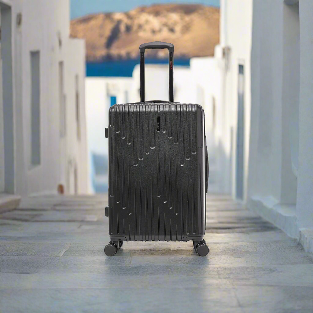 Black suitcase on wheels in a sunlit outdoor setting with white buildings and blue sky.