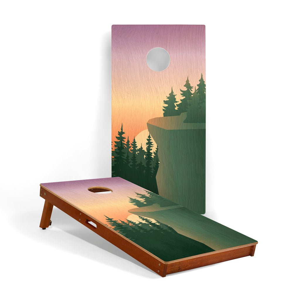 Cornhole board with nature-themed design featuring trees and a sunset