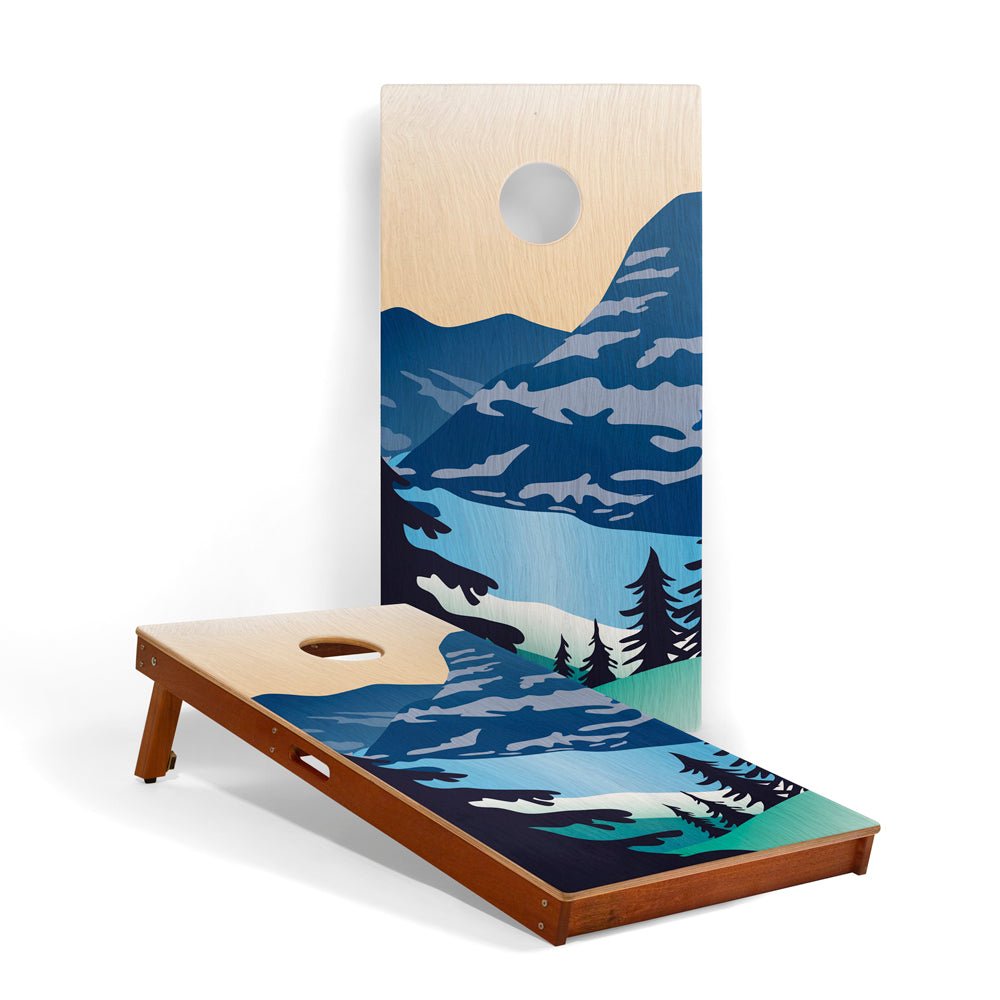 Cornhole board with nature-themed design featuring mountains and trees on a white background