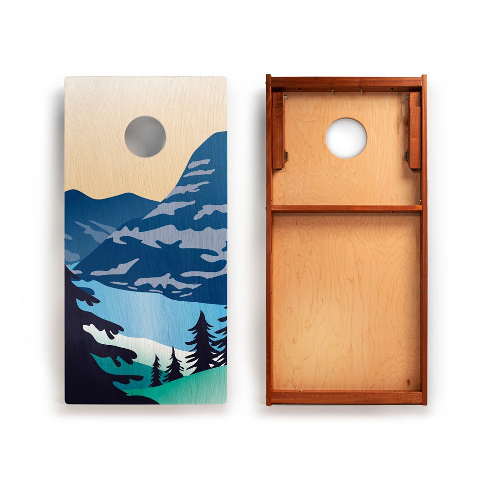 Wooden cornhole board with mountain and lake design on one side and plain wood on the other, on a white background.