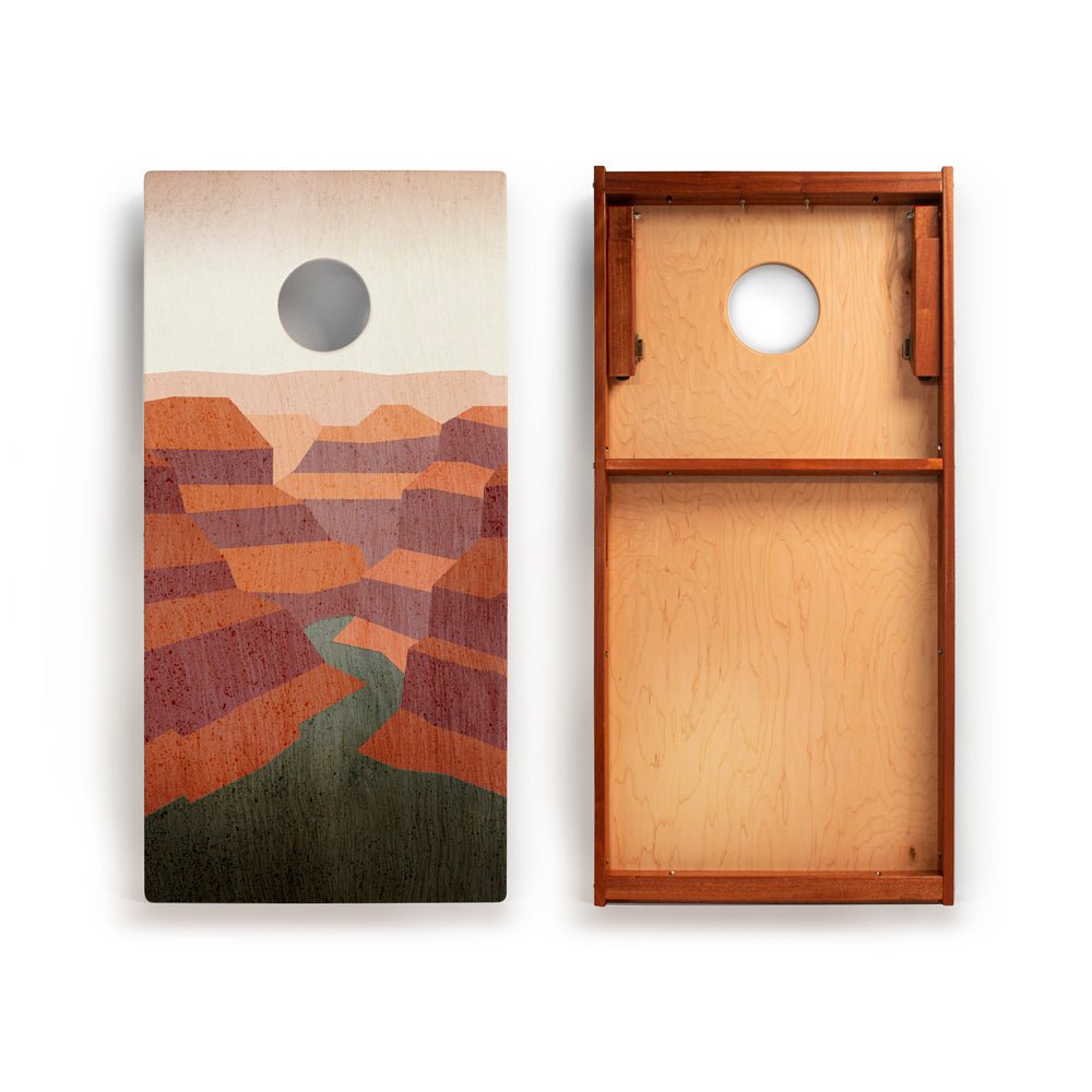Two cornhole boards with one featuring a landscape design and the other showing the back.