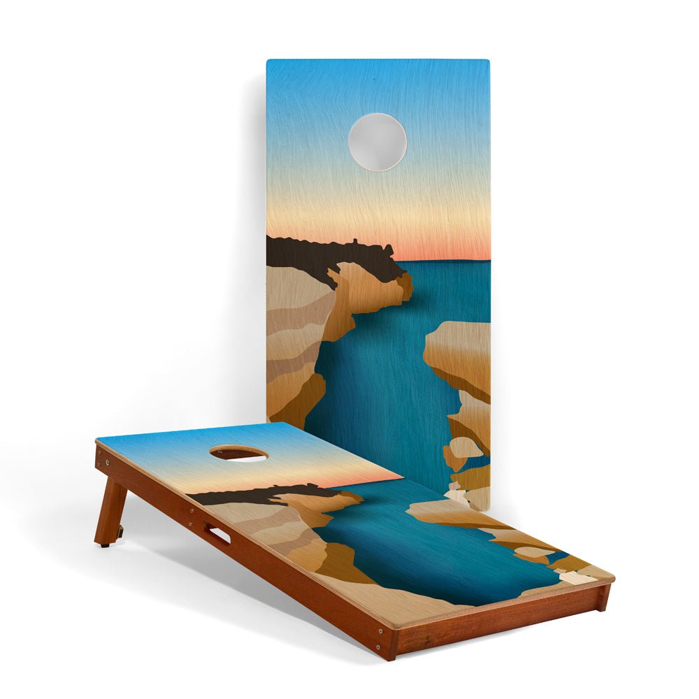 Cornhole board with a beach scene design featuring a sunset over water and cliffs.