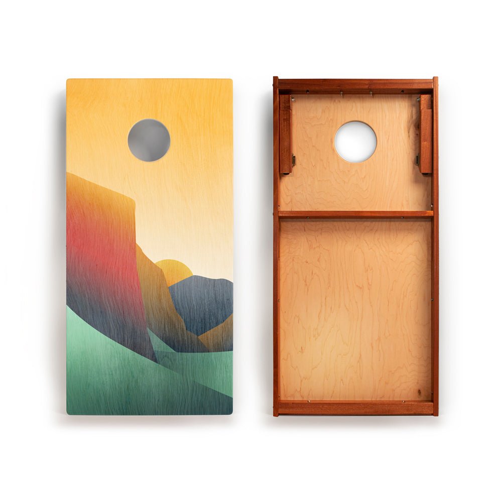Cornhole board with colorful mountain design on one side and wooden texture on the other, on a white background.