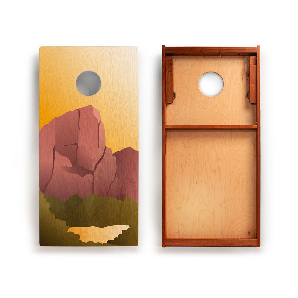 Two wooden cornhole boards with a mountain design on one and a plain wood surface on the other.