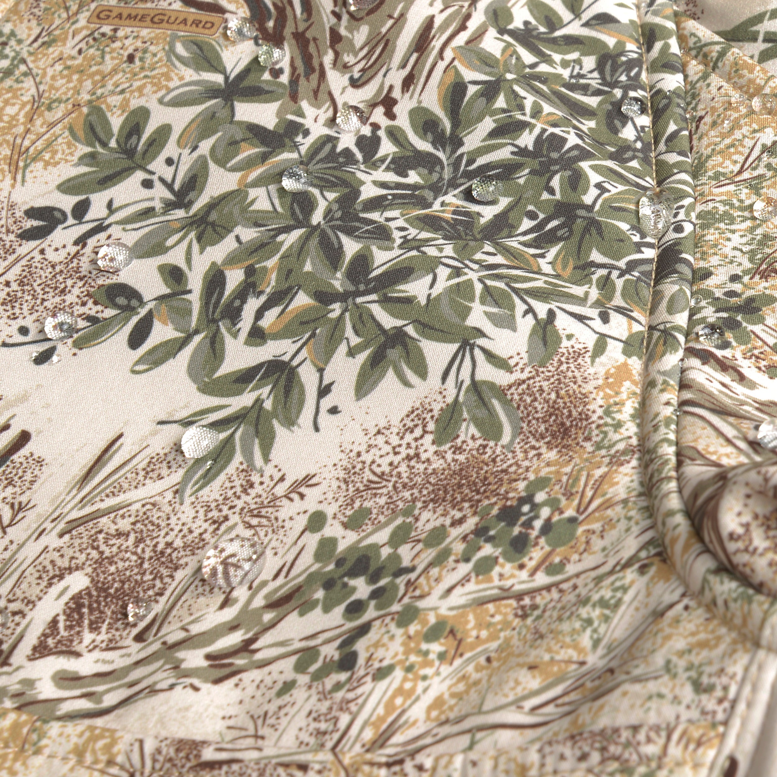 Close-up of a camouflage fabric with leaf patterns, featuring the GameGuard brand.