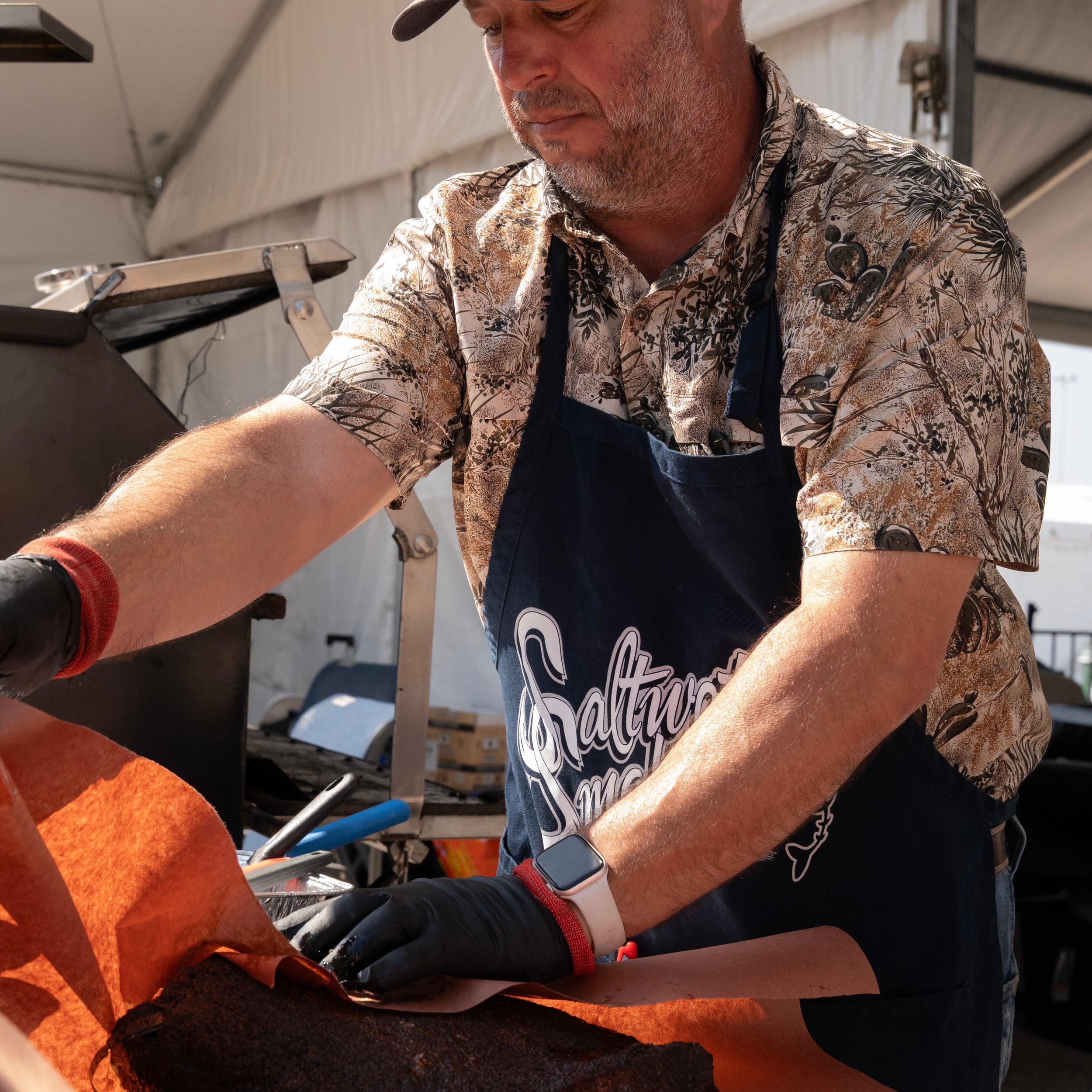 Man wearing a patterned shirt and apron, working on a project with tools.