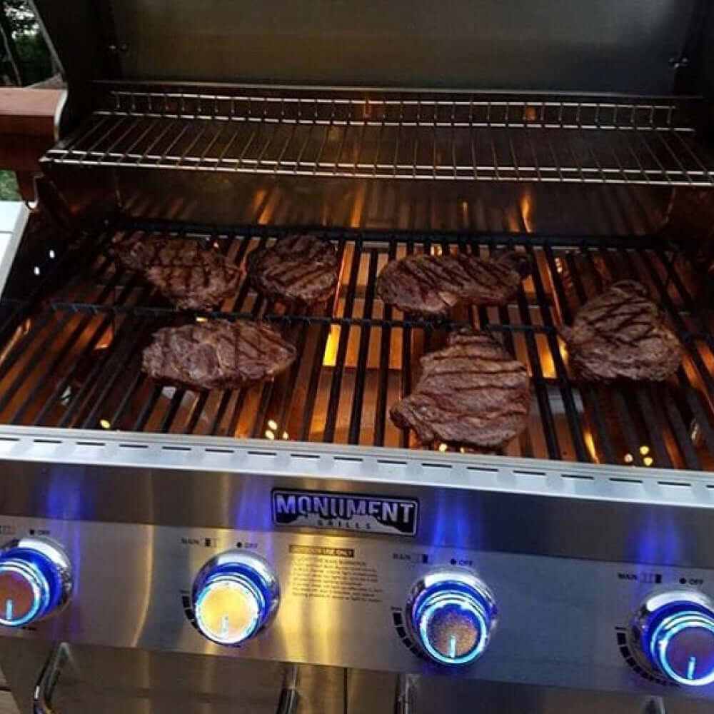 Grill with hamburgers cooking on the grates, brand 'Monument Grills' visible.