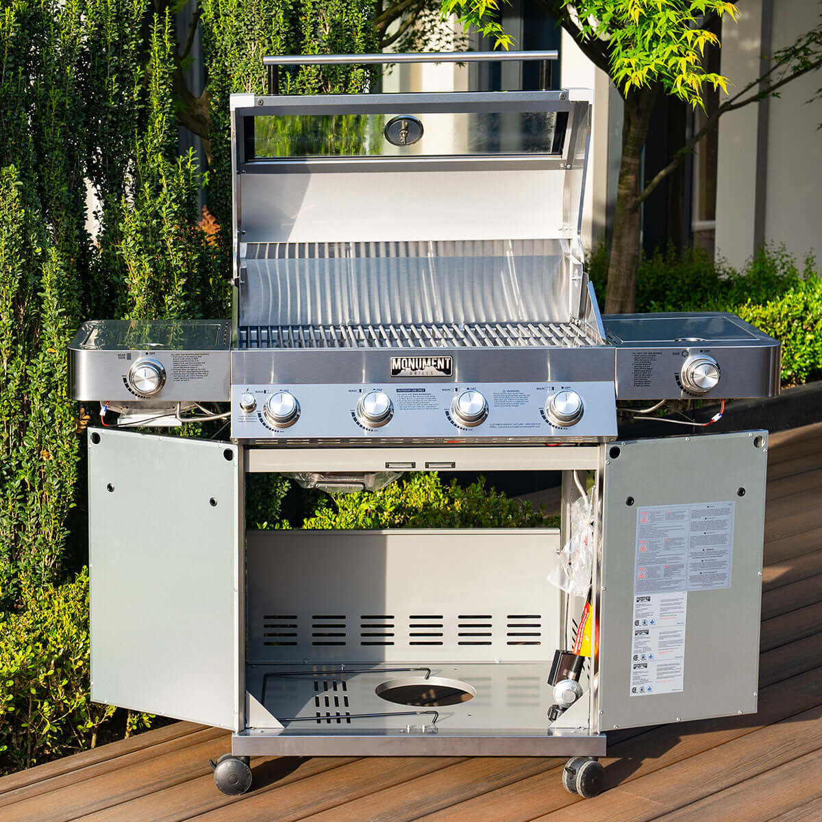 Stainless steel barbecue grill on a wooden deck with greenery in the background
