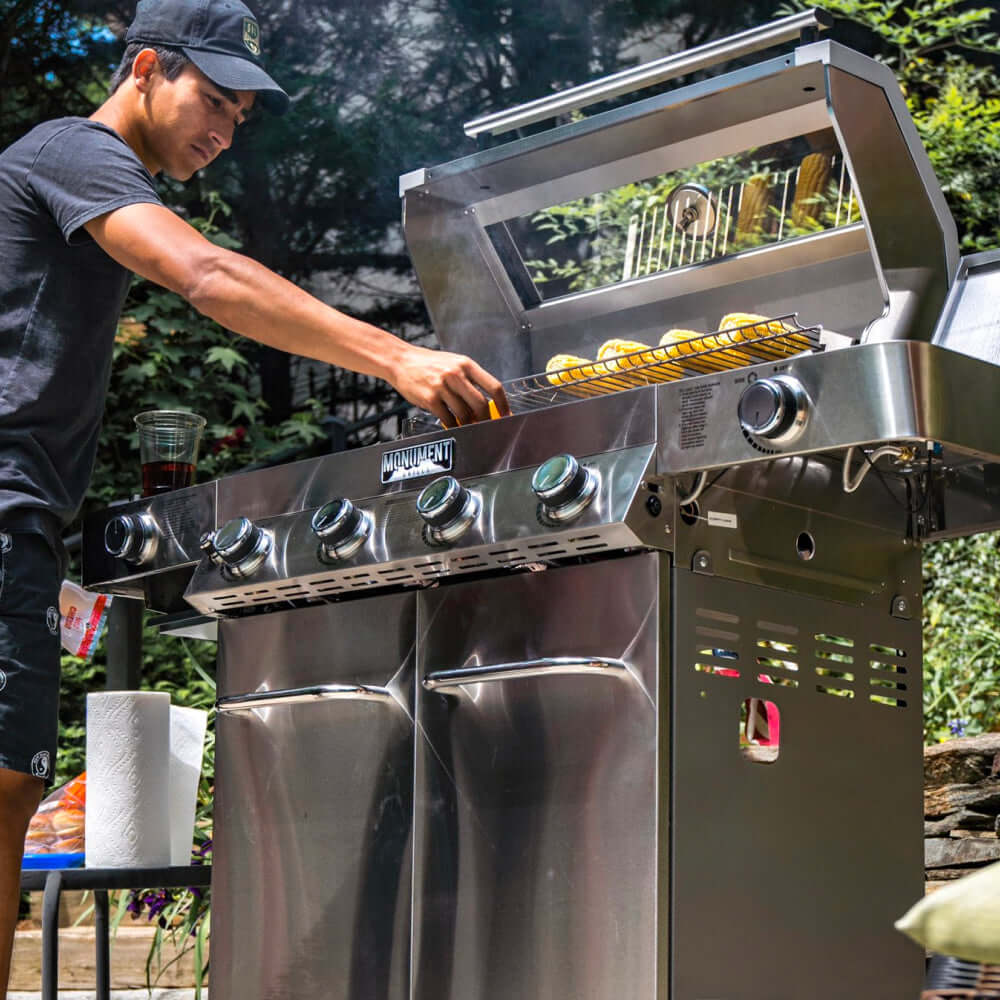 Person grilling outdoors using a large stainless steel barbecue grill.