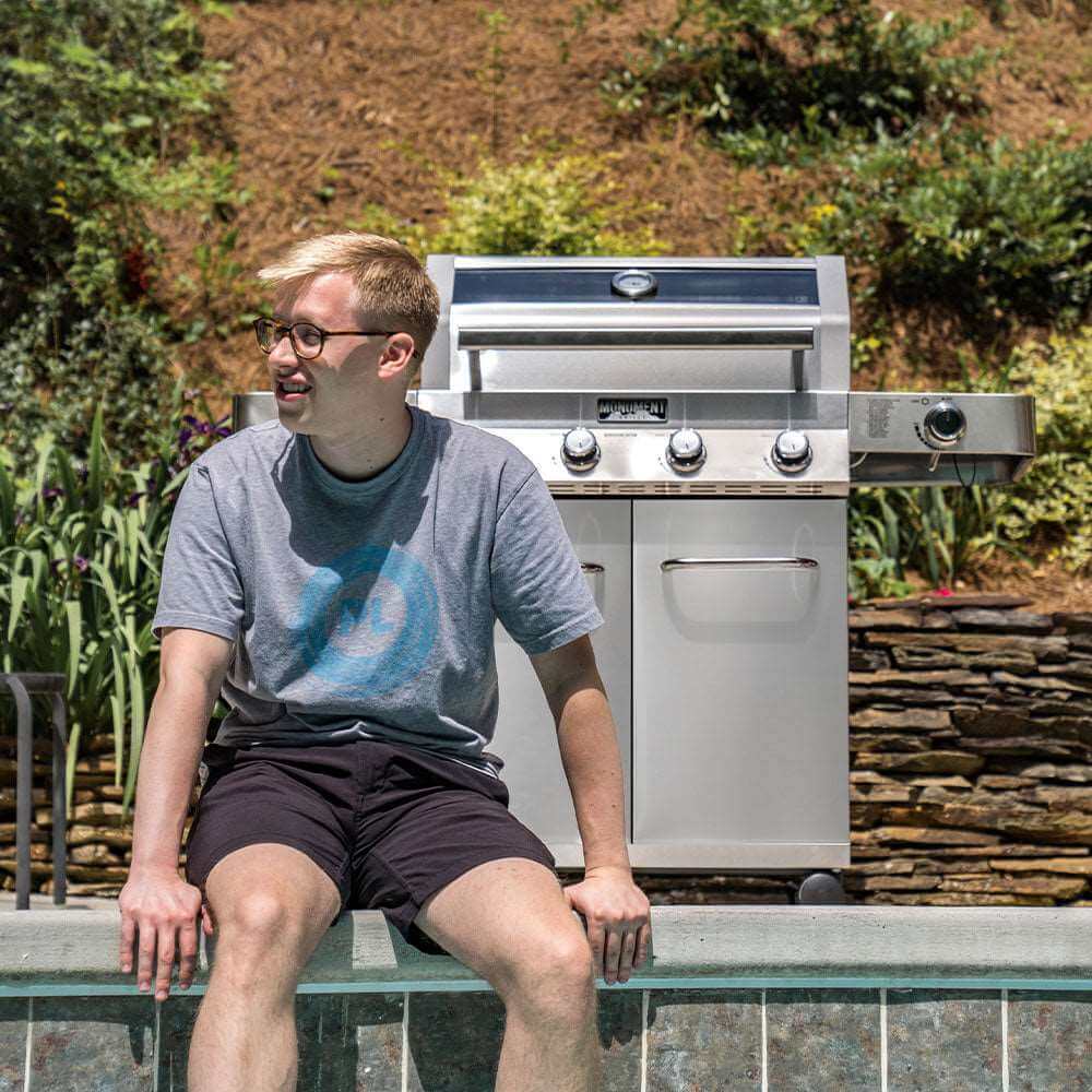 Person sitting on a ledge with a stainless steel grill in the background
