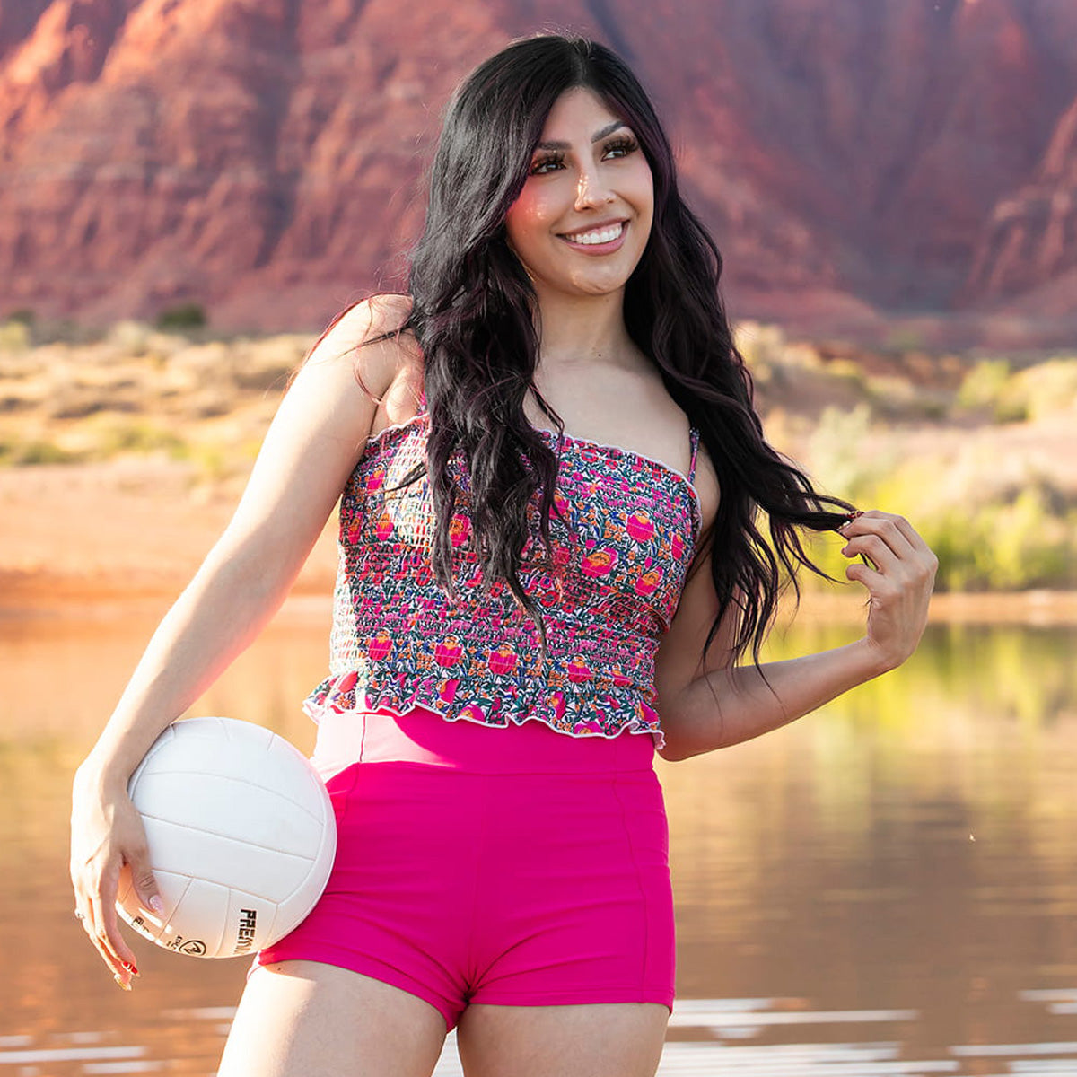 Woman holding a volleyball by a lake with mountains in the background