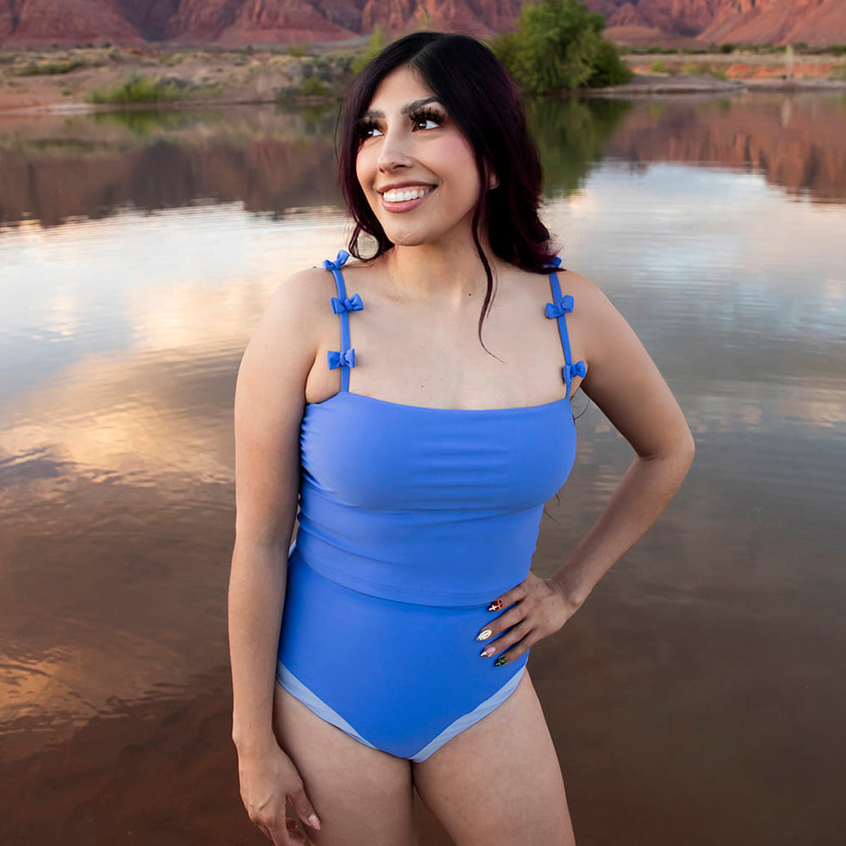 Woman in a blue swimsuit standing by a body of water with mountains in the background