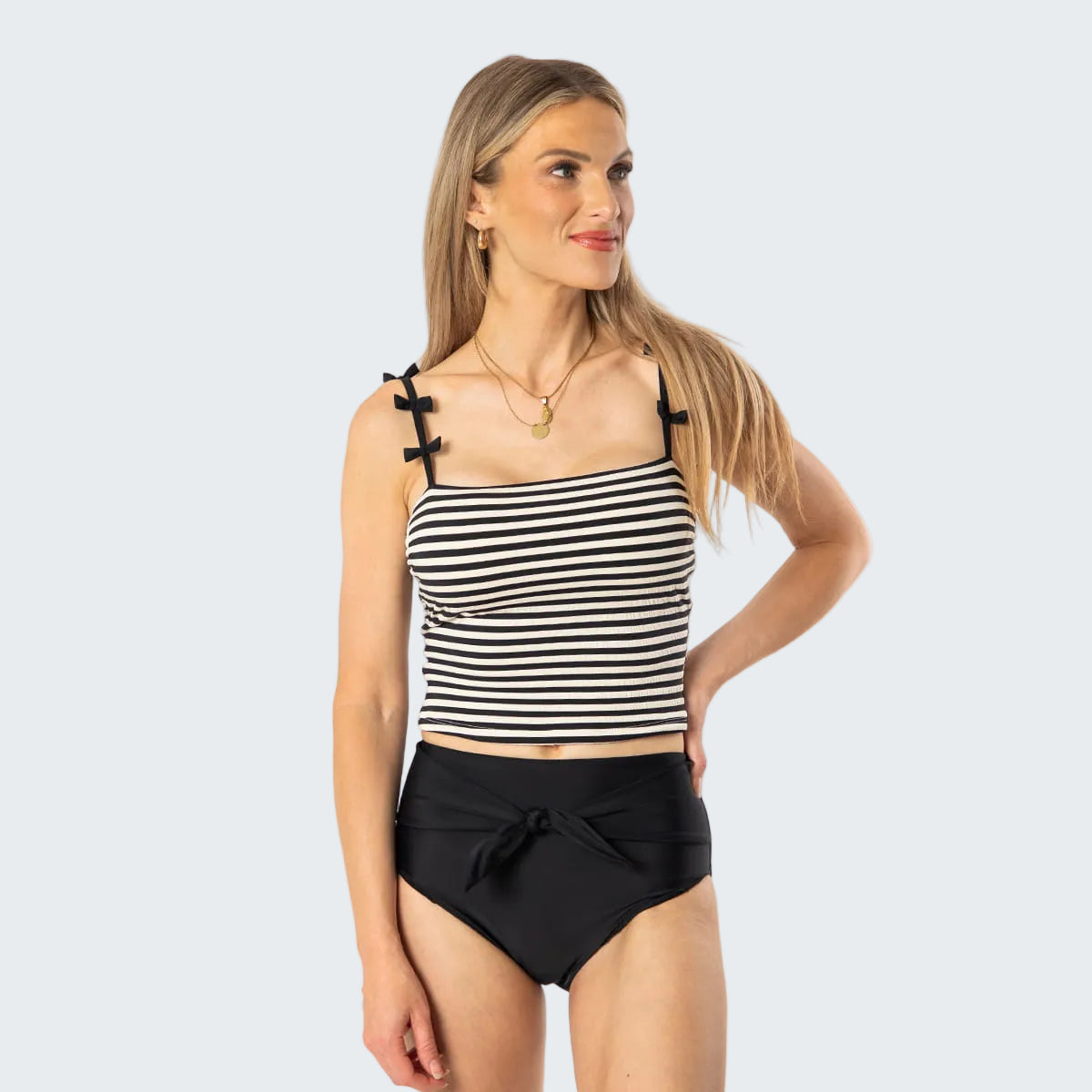 Woman wearing a black and white striped tank top and black high-waisted shorts on a white background