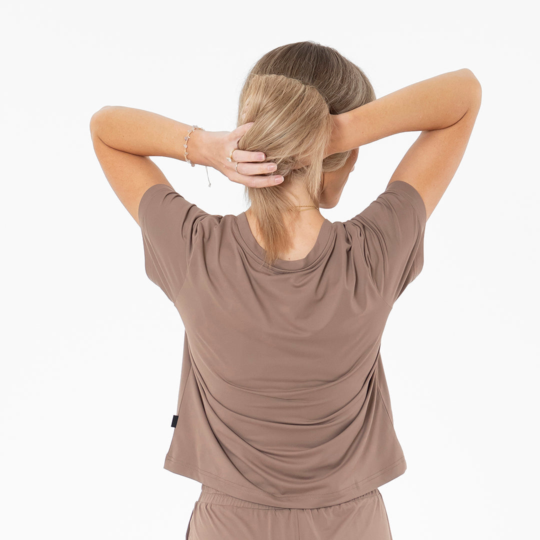 Woman wearing a brown athletic outfit with her back to the camera on a white background