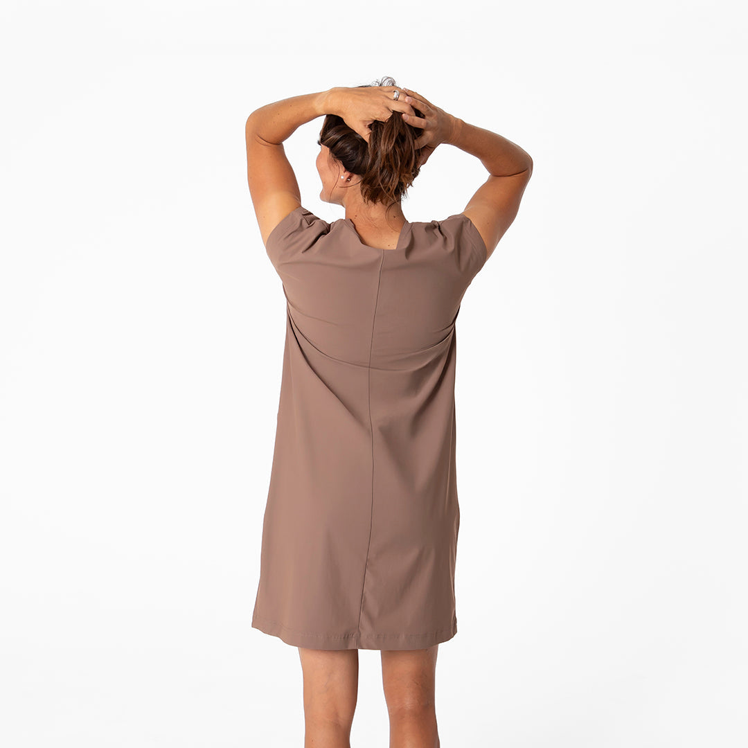 Woman wearing a brown dress with her hands behind her head on a white background