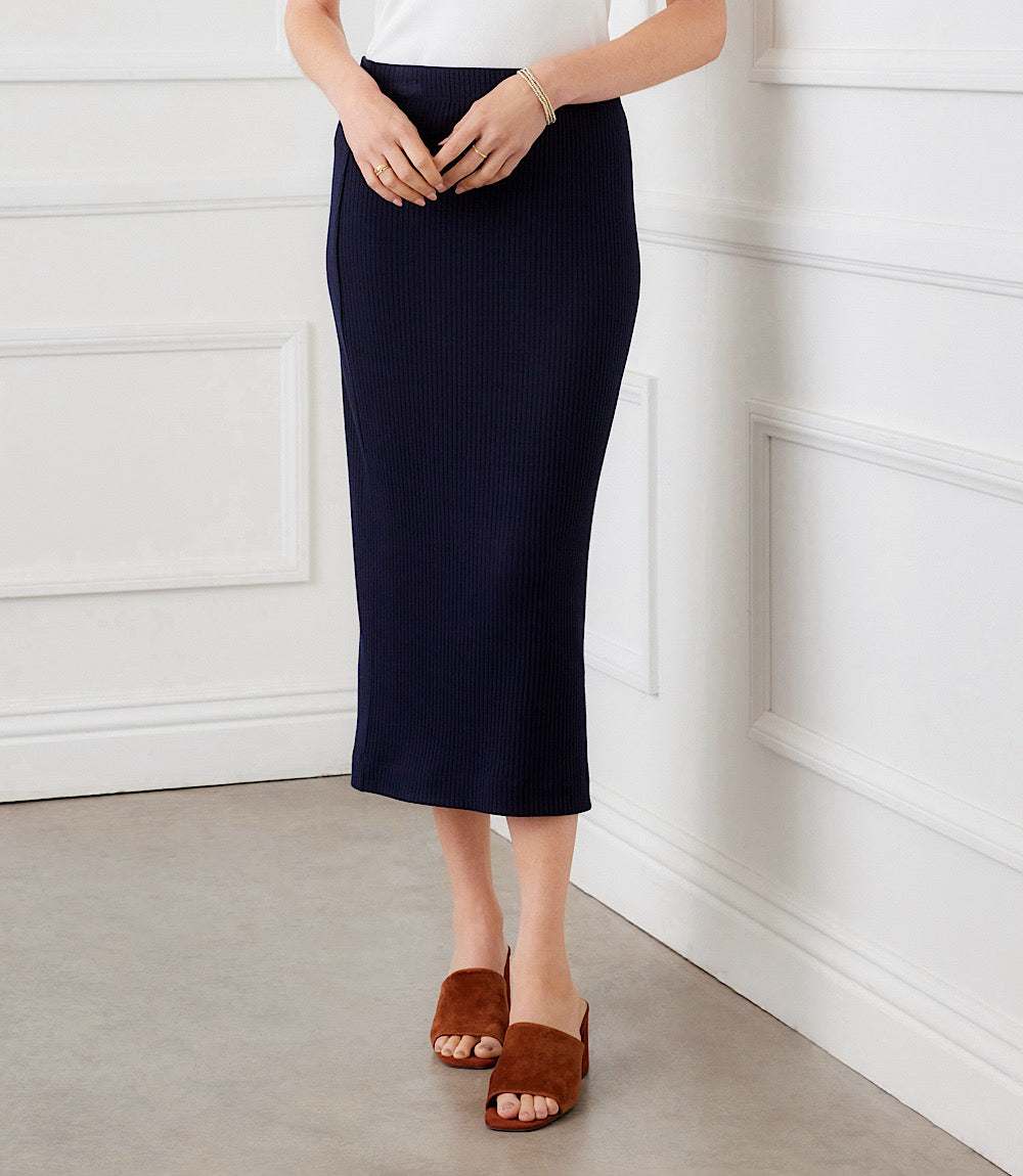 Person wearing a navy skirt and brown sandals against a white paneled wall.