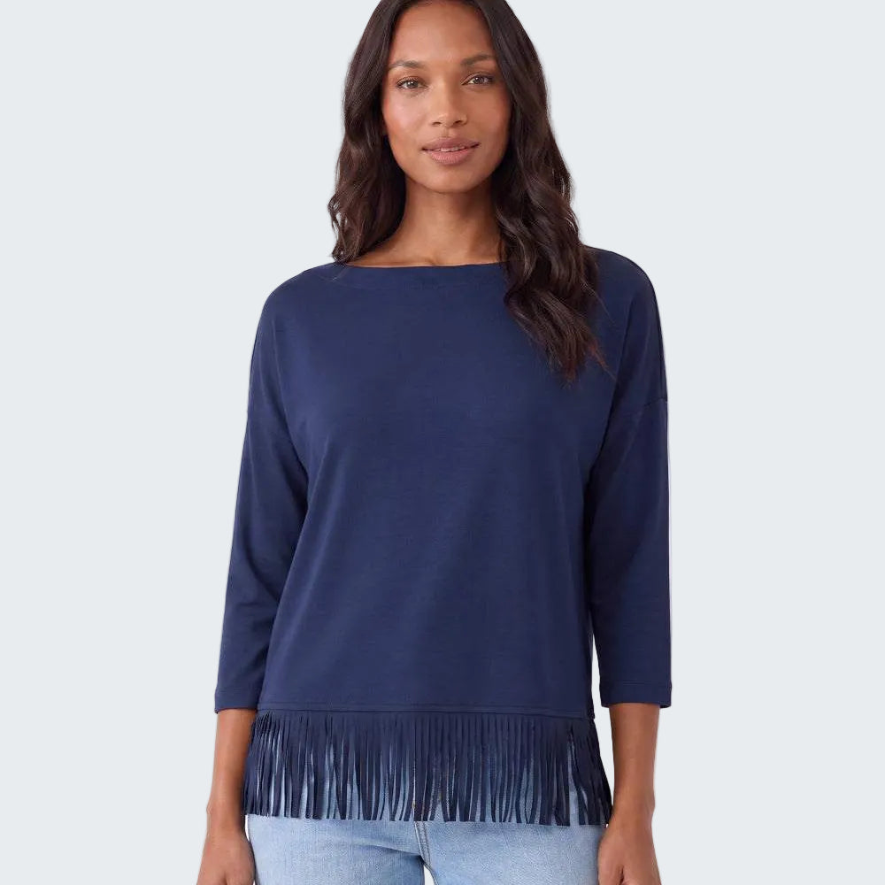 A woman modeling a navy blue long-sleeve top with fringe trim at the hem, paired with light blue jeans, against a plain white studio background.