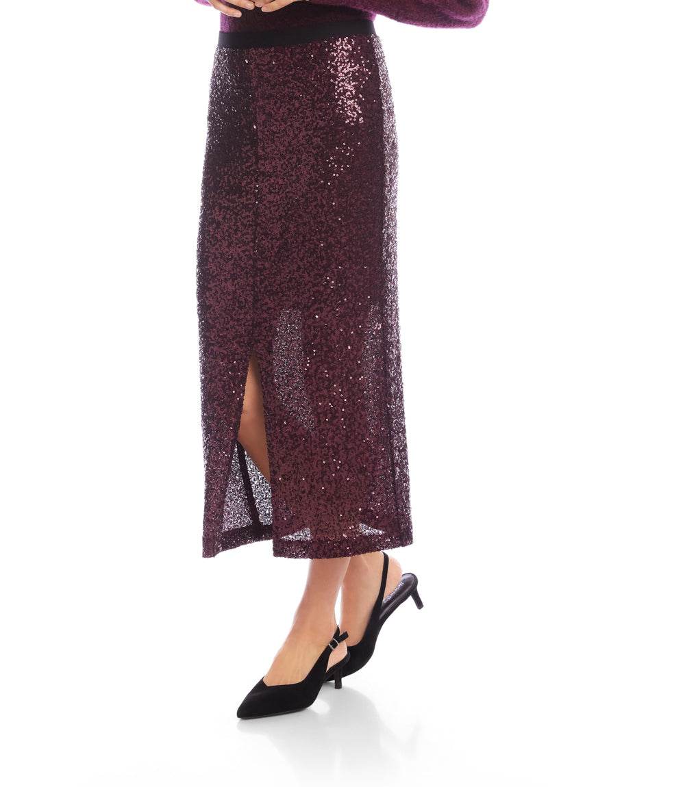 A model wearing a sparkling dark plum sequin midi skirt with a front slit, paired with black slingback heels, shown against a plain white background.