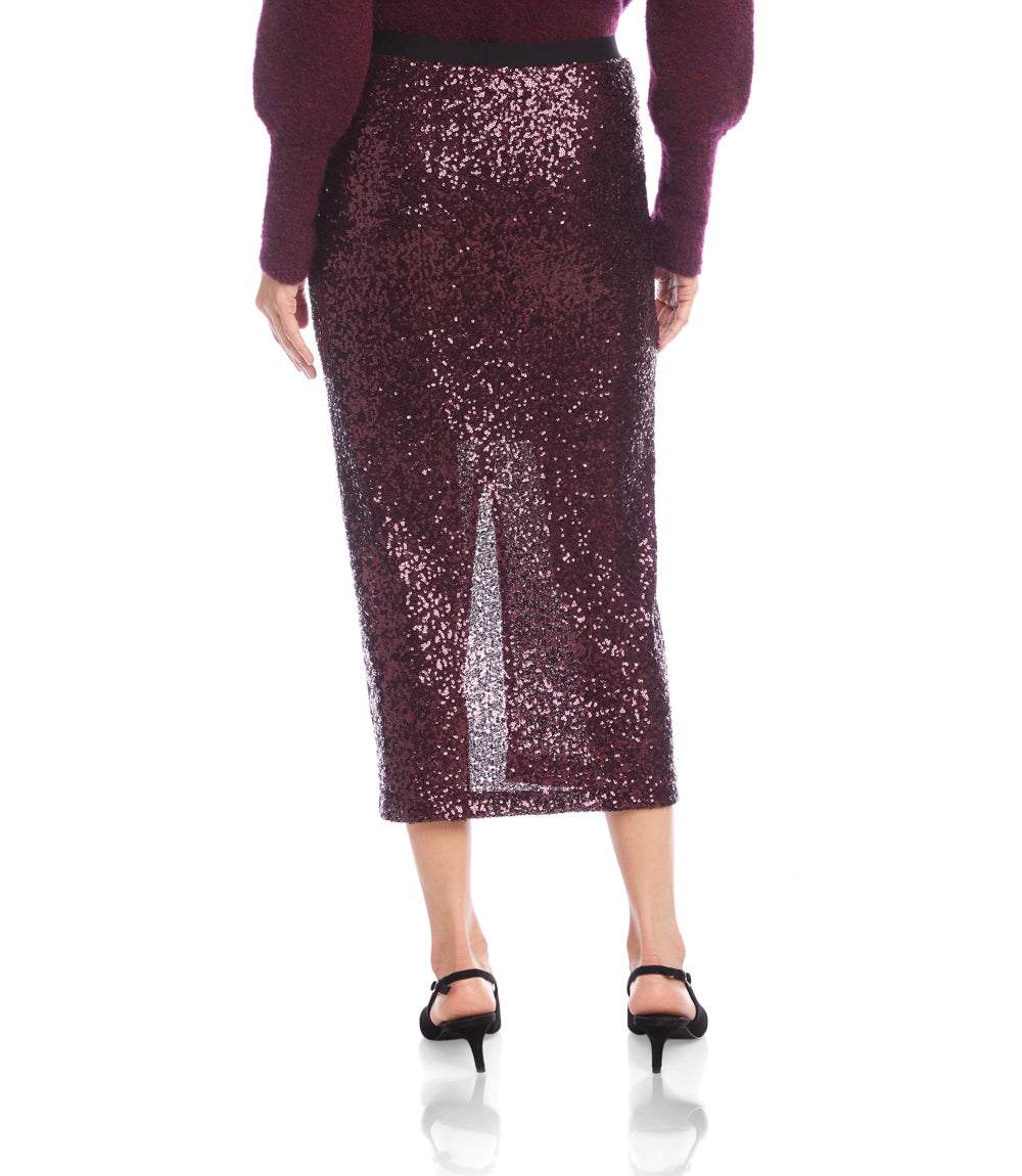 A model wearing a sparkling burgundy sequin midi skirt with a front slit, paired with a matching burgundy top and black heeled sandals, shown against a plain white background.