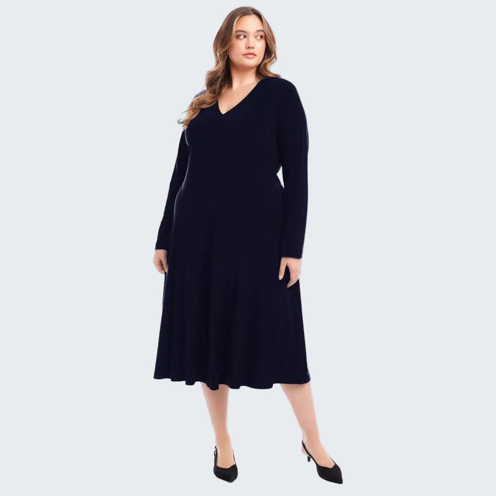 A woman modeling a long-sleeve, V-neck, knee-length black dress with a flared skirt, paired with black pointed-toe heels, against a solid white background.
