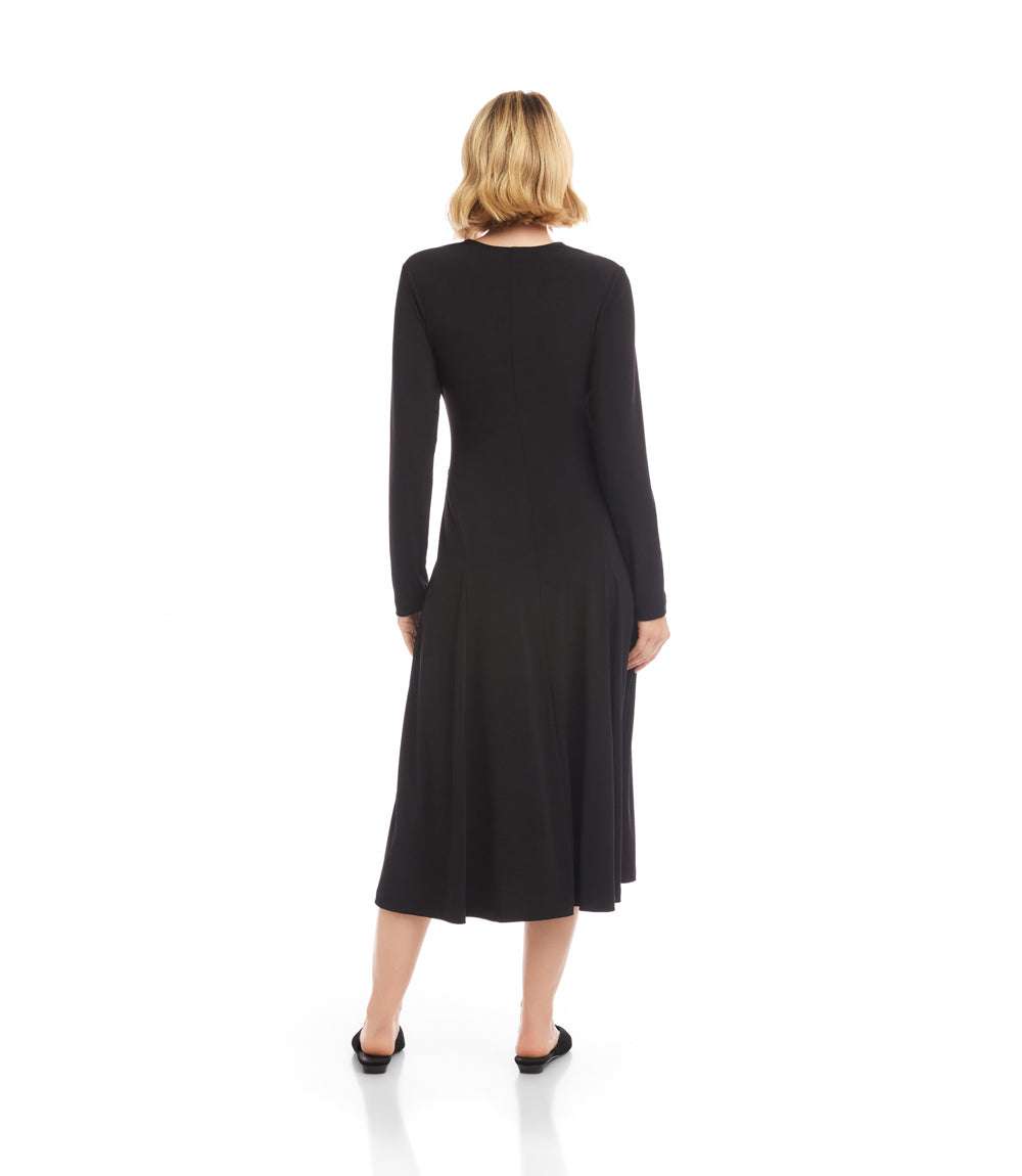 A woman viewed from the back wearing a black long-sleeve midi dress and black flats against a plain white studio background.