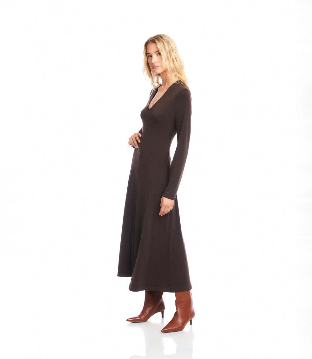 A woman modeling a long-sleeve, V-neck maxi dress in dark brown, paired with brown ankle boots, against a solid white studio background.