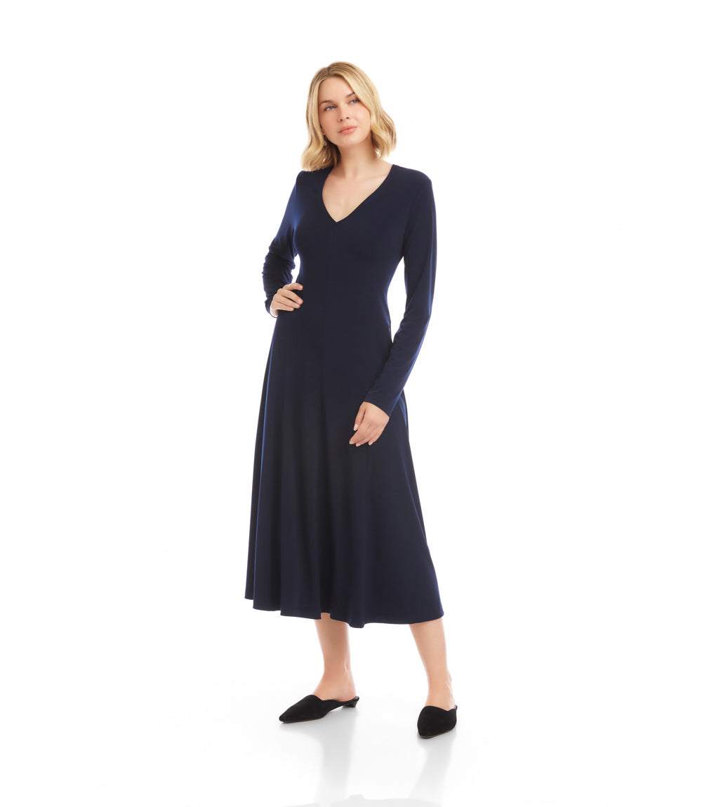 A woman modeling a long-sleeve navy blue midi dress with a V-neckline, standing against a plain white studio background.