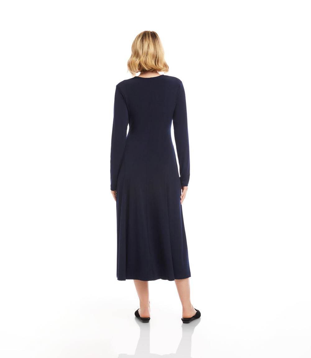 A woman viewed from the back wearing a long-sleeve navy midi dress and black flats, standing against a plain white studio background.