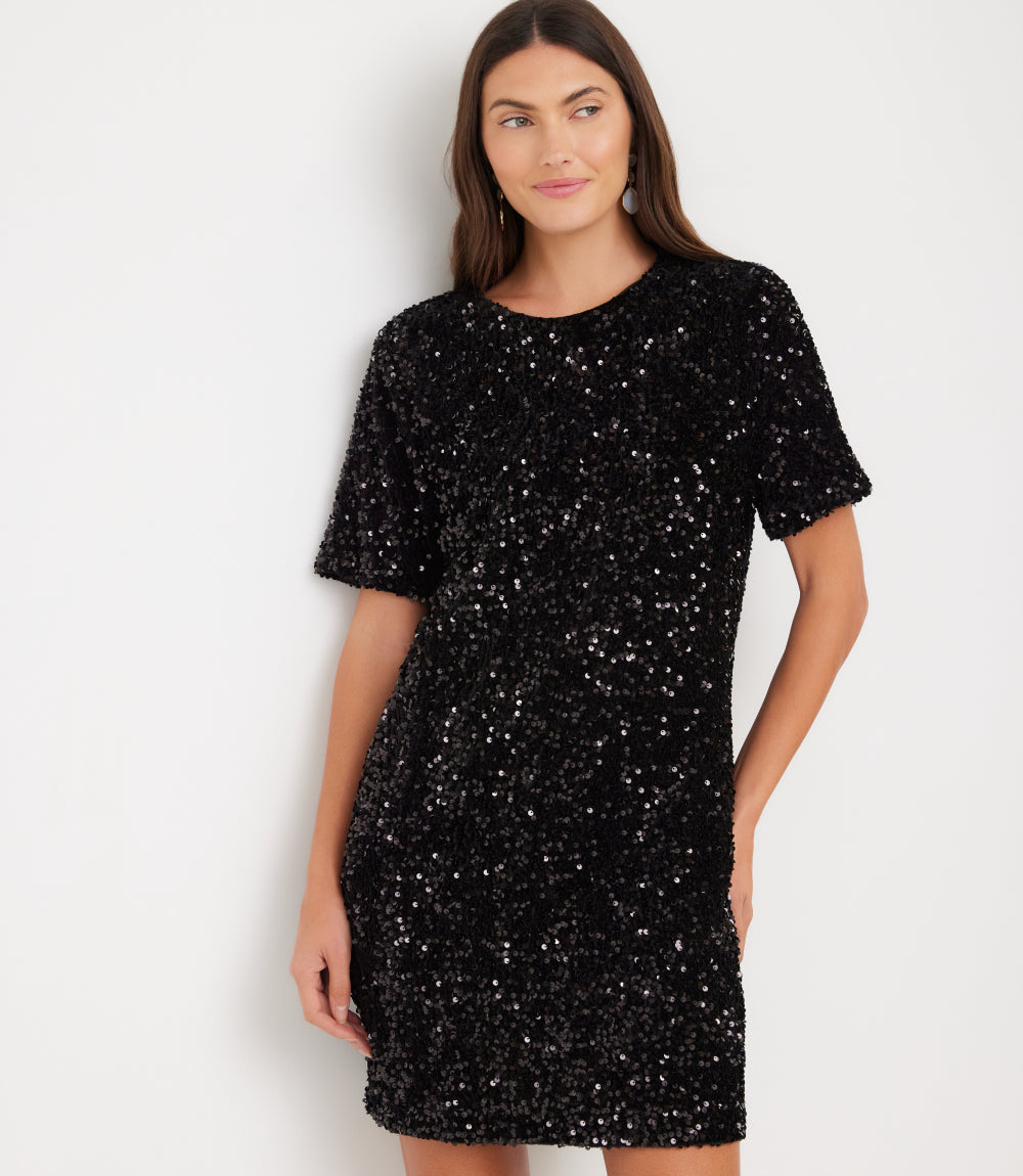 A woman modeling a short-sleeve black sequined dress against a plain white studio background.