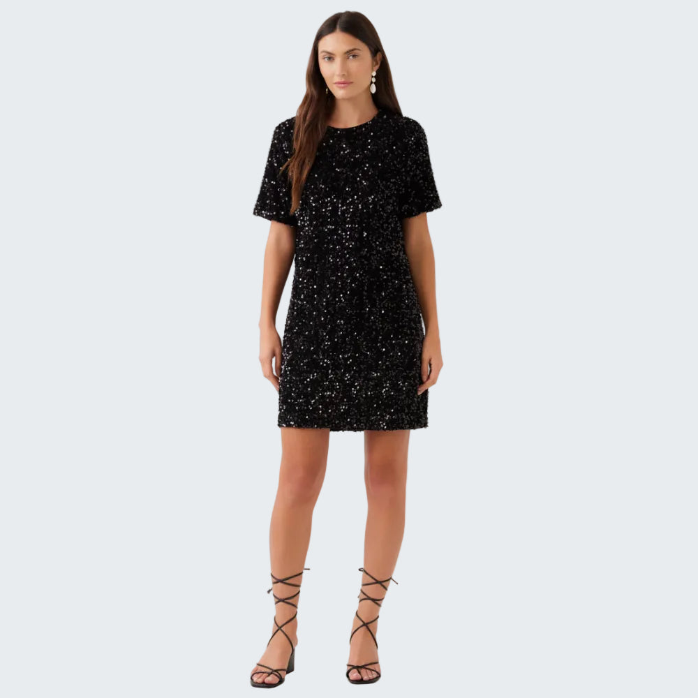 A woman modeling a short-sleeve black sequined mini dress with a crew neck, paired with black lace-up heeled sandals, against a plain white studio background.