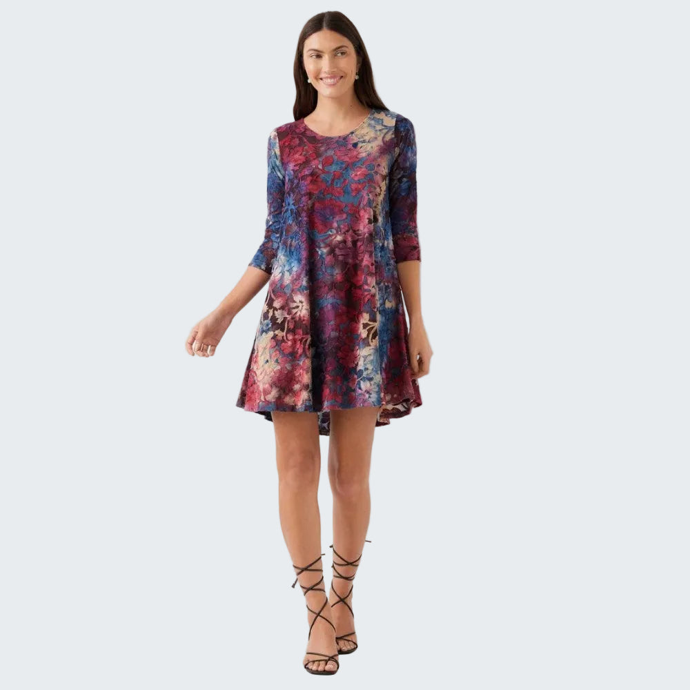 A woman modeling a short, three-quarter sleeve skater dress with a vibrant abstract floral print in shades of blue, purple, and red, paired with black lace-up heeled sandals against a plain white studio background.