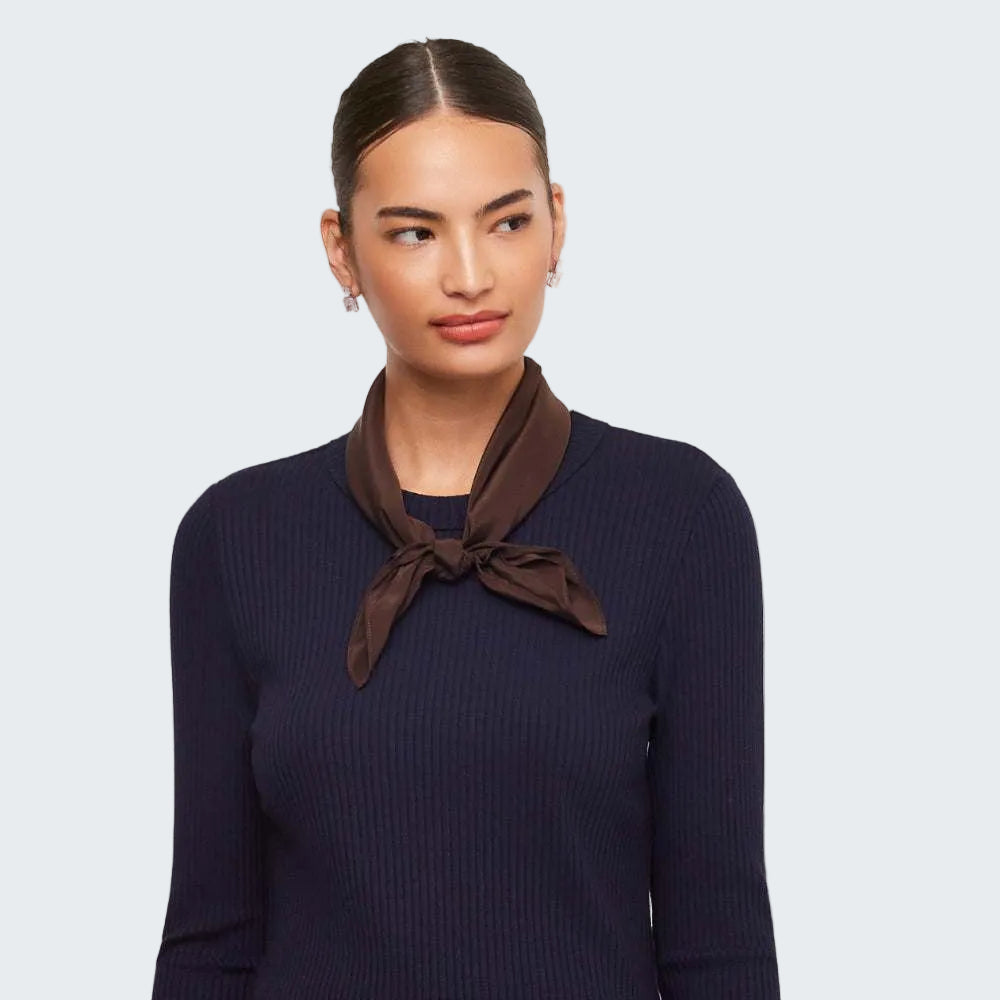 A woman wearing a dark navy ribbed long-sleeve top and a dark brown satin neck scarf tied in a knot at the collar, photographed against a plain light gray studio background.