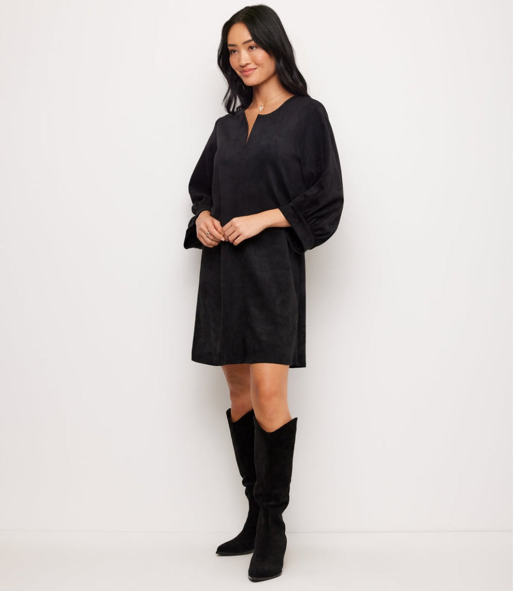 A woman modeling a black long-sleeve mini dress with a split neckline, paired with black knee-high boots, against a plain white studio background.