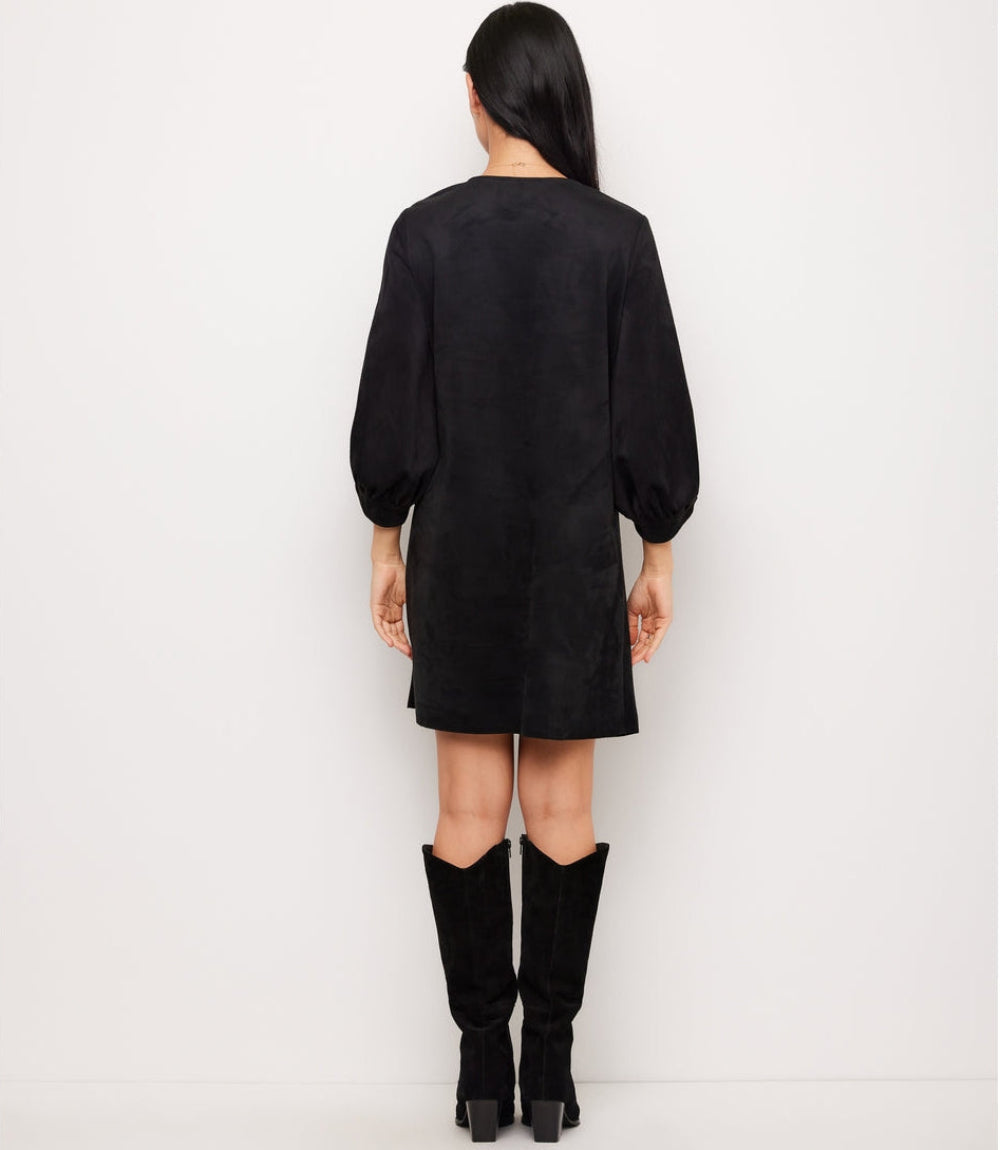 A woman viewed from the back wearing a black long-sleeve puff-sleeve mini dress and black knee-high boots against a plain white studio background.