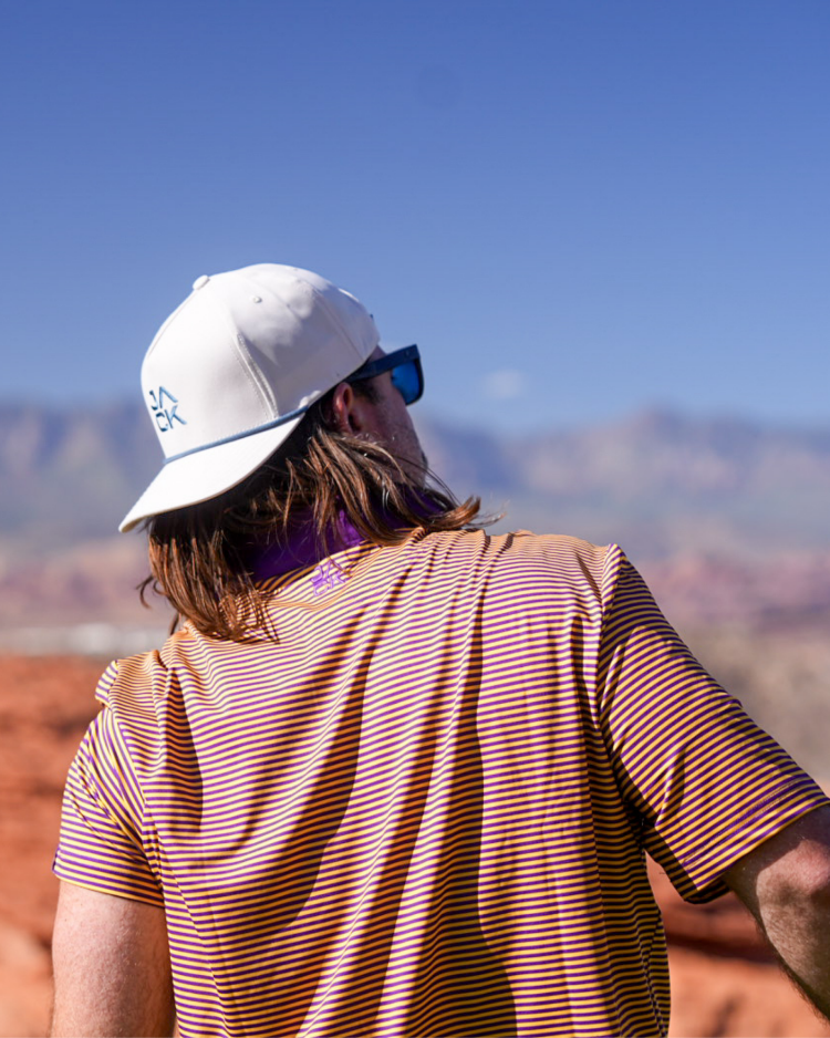 Person wearing a white cap and striped shirt, looking at mountains with a clear blue sky.