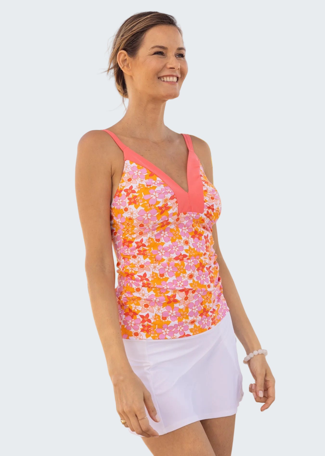 Woman wearing a colorful floral tank top and white skirt on a beach with palm trees in the background.