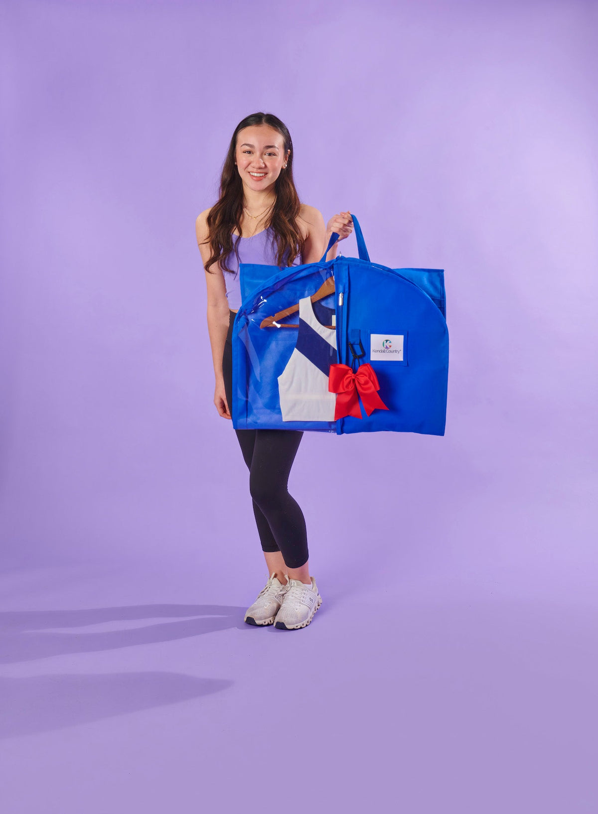 Person holding a blue tote bag with a red bow against a purple background