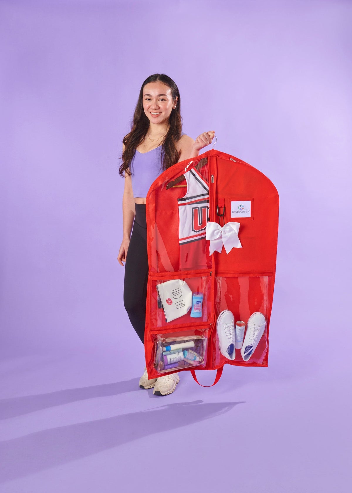 Person holding a red garment bag with various items on a purple background