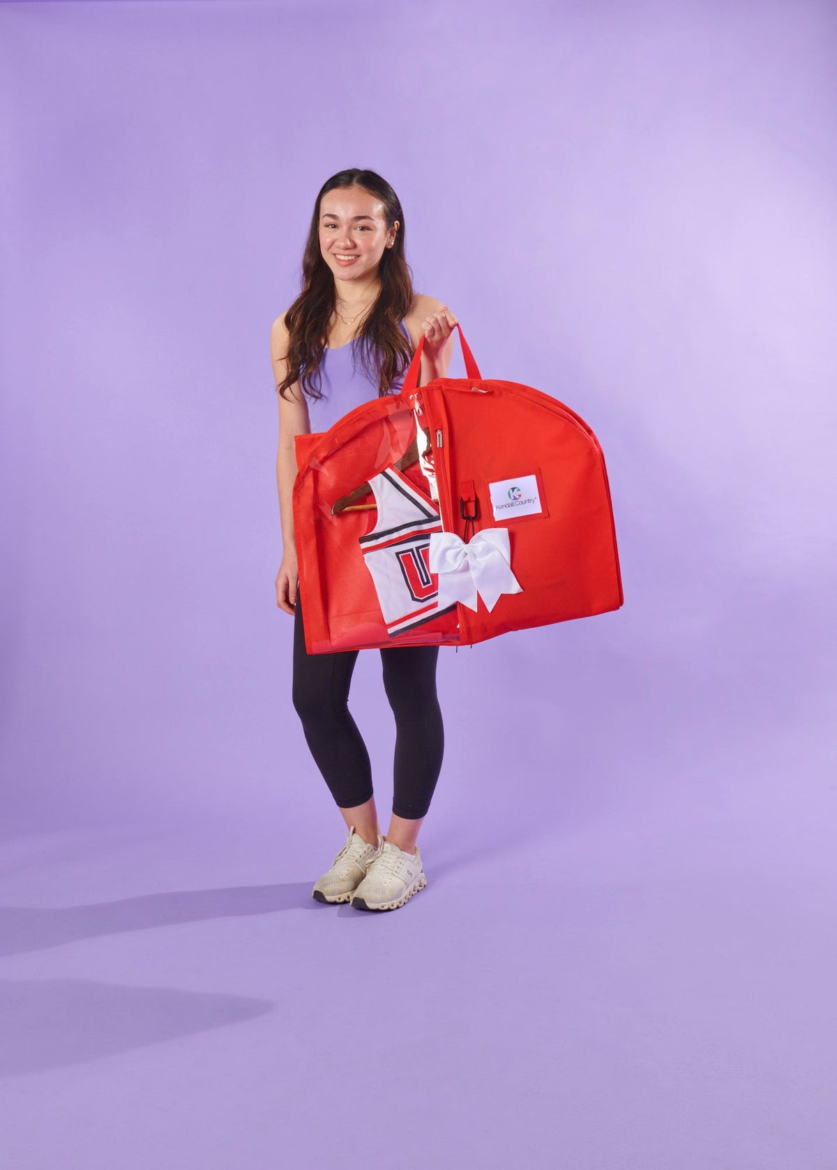 Person holding a red garment bag with a white bow on a purple background