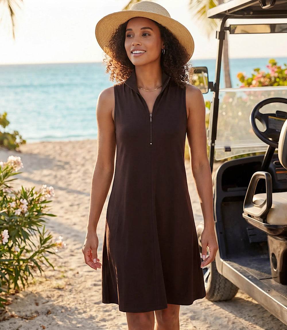 Woman in a black dress and sun hat standing on a beach with ocean view