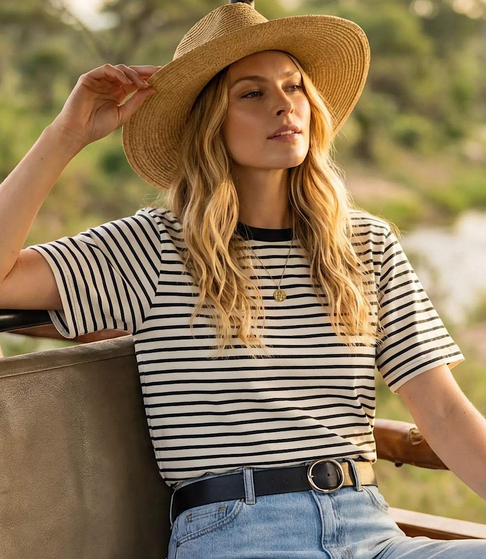 Woman wearing a straw hat, striped shirt, and jeans sitting outdoors.