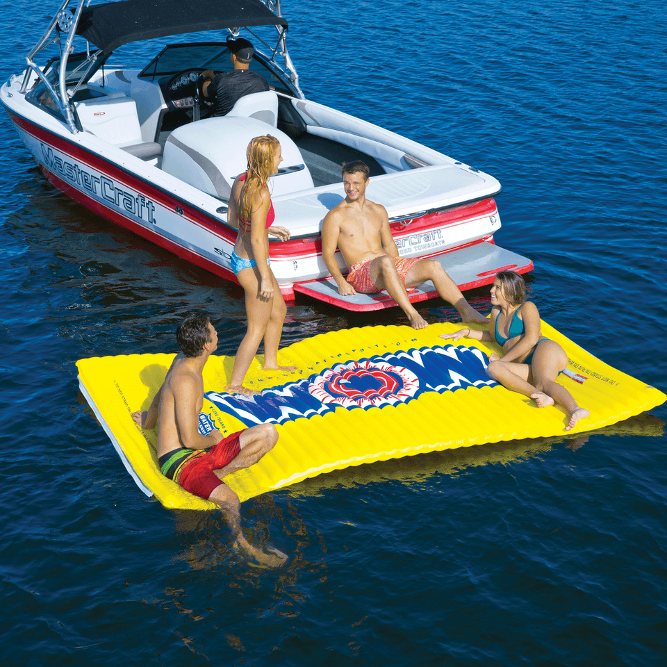 People on a yellow inflatable raft in the water with a boat in the background.