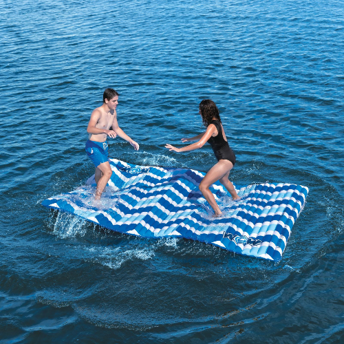 Two people playing on a blue and white striped inflatable raft in the ocean.