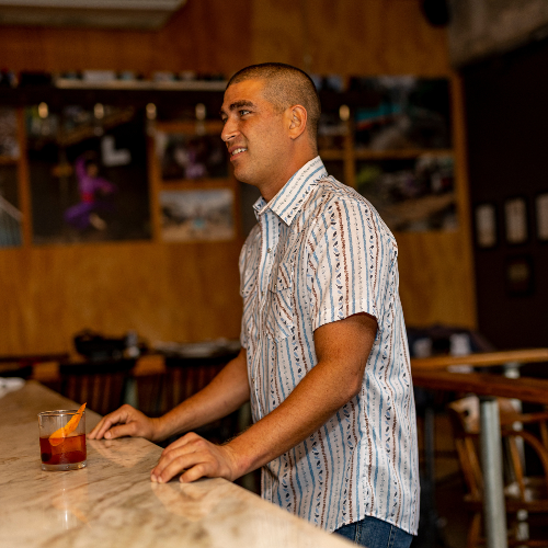 Man standing at a bar with a drink in a casual setting