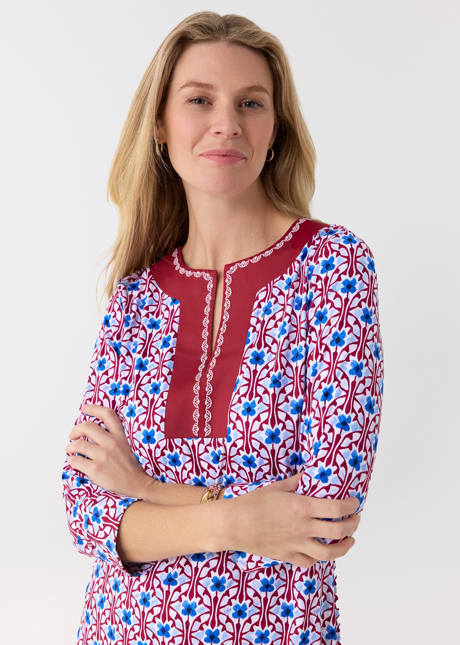 Woman wearing a patterned top with red, blue, and white design on a plain background