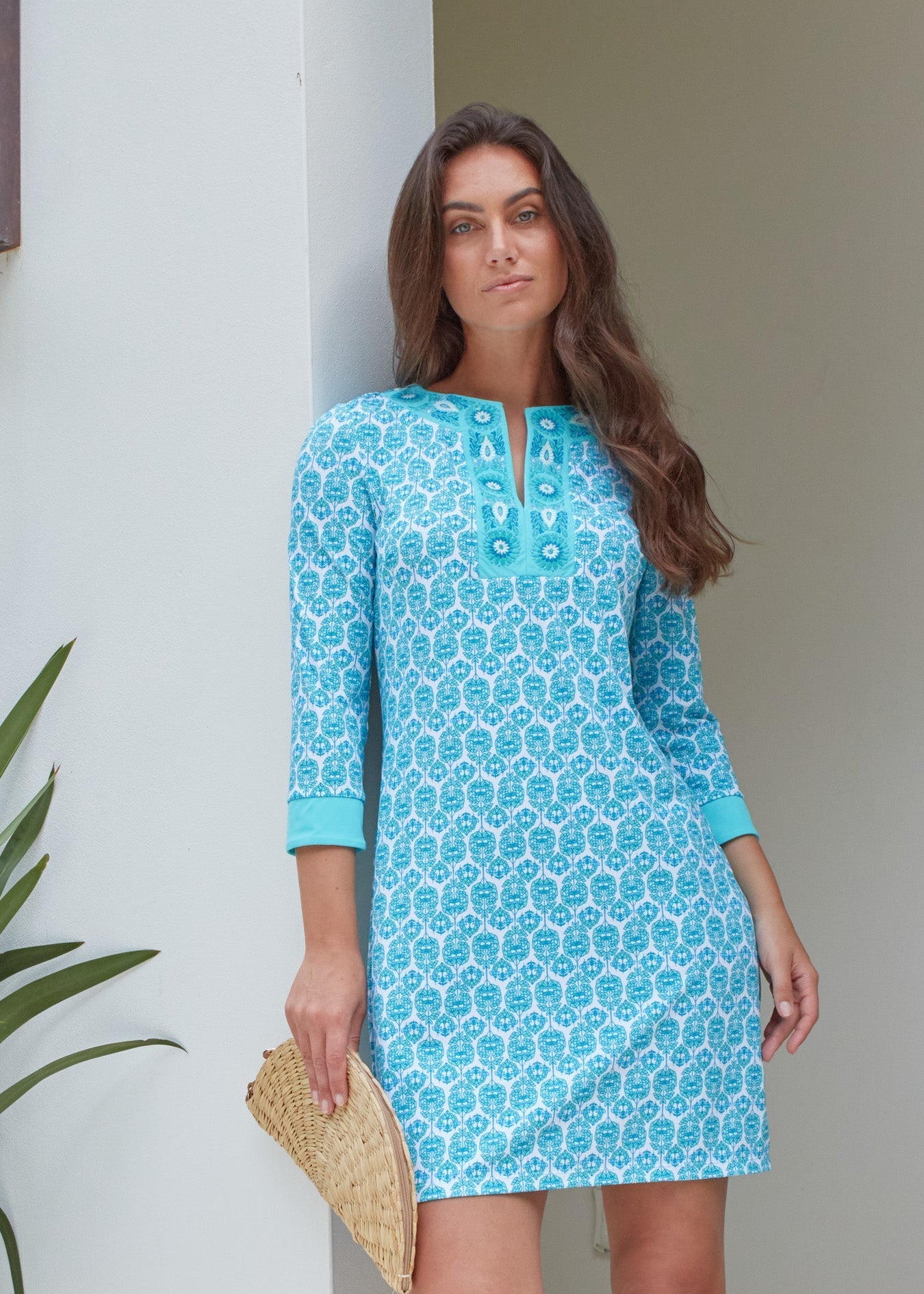 Woman wearing a blue patterned dress standing against a white wall.